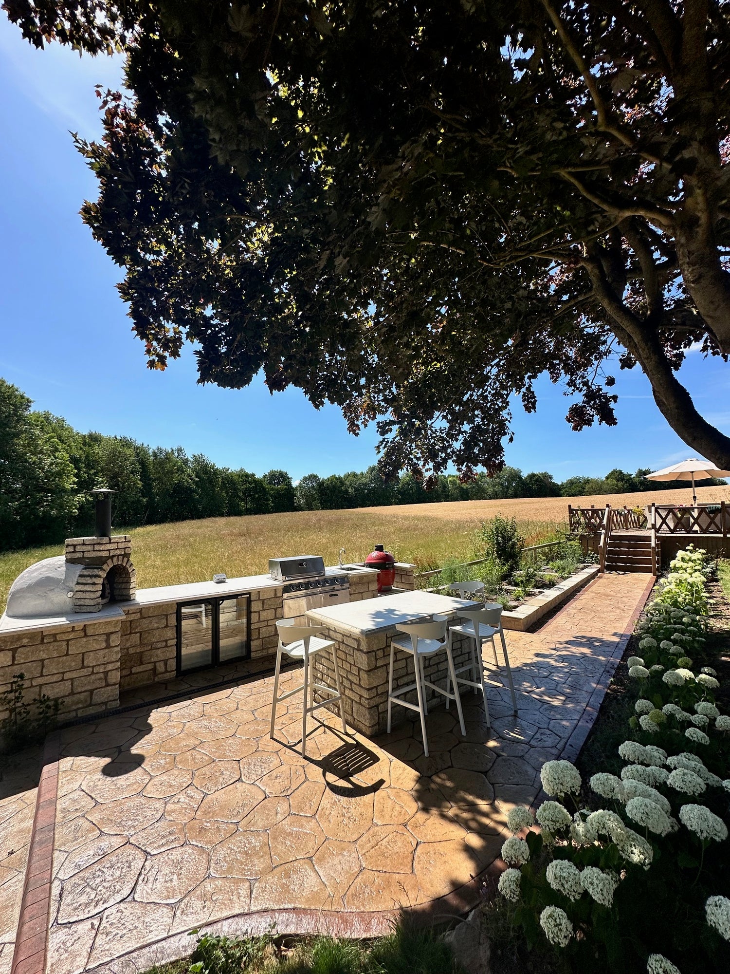 Outdoor patio area with chairs and tables on a stone patio, surrounded by trees and greenery.